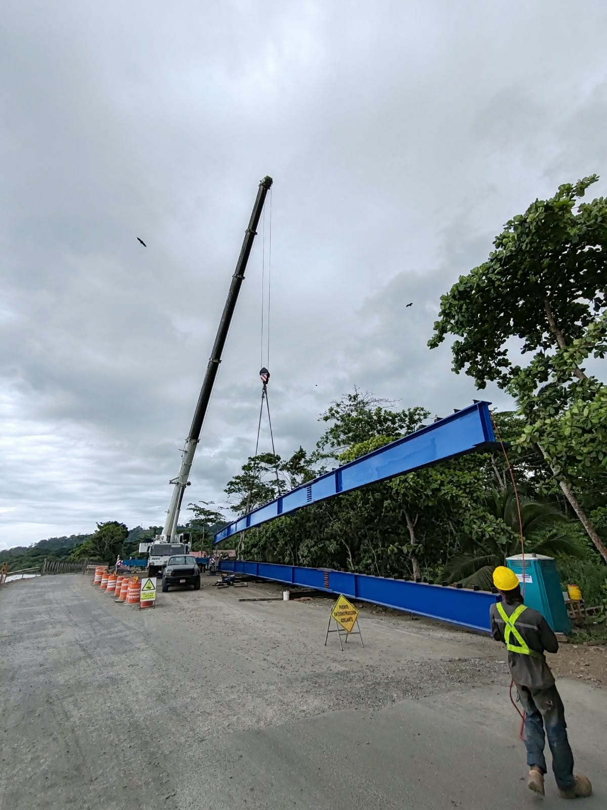 Grúa izando una viga metálica azul junto a una carretera en Puerto Viejo, Limón.